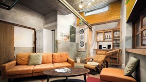 Un salon moderne avec un canapé en cuir, une table basse ronde, un fauteuil en osier et une bibliothèque.