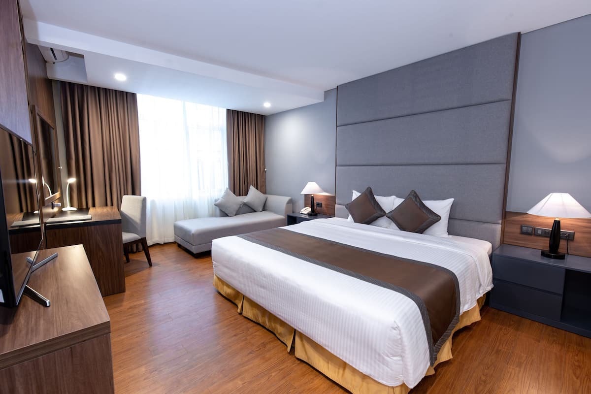 Una habitación de hotel moderna con una cama grande, un escritorio, un sofá y una mesita de noche con lámparas.