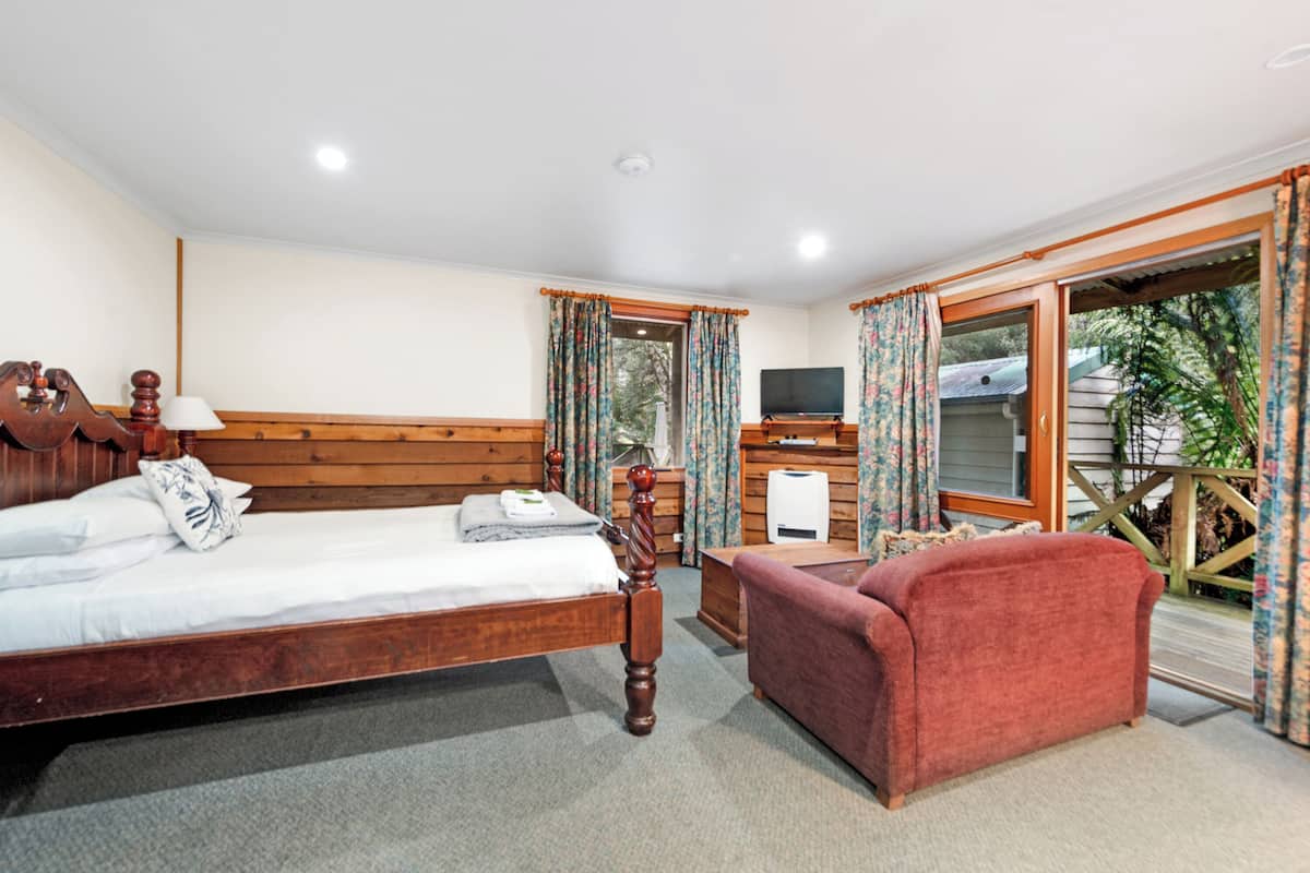A bedroom with a wooden bed, a red sofa, a TV, and a window with curtains.