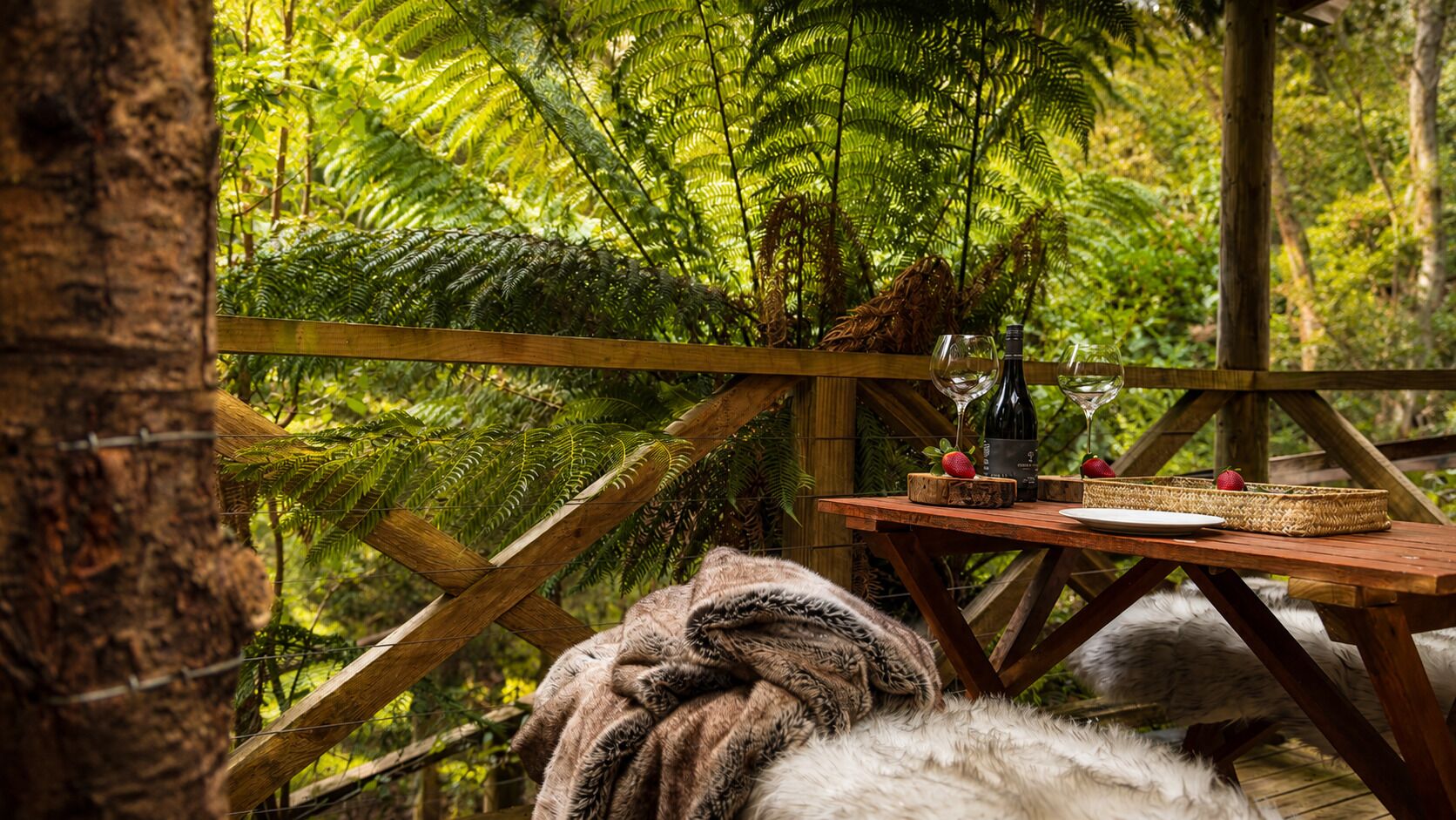 Un patio in legno con un tavolo apparecchiato per mangiare, immerso nel verde.