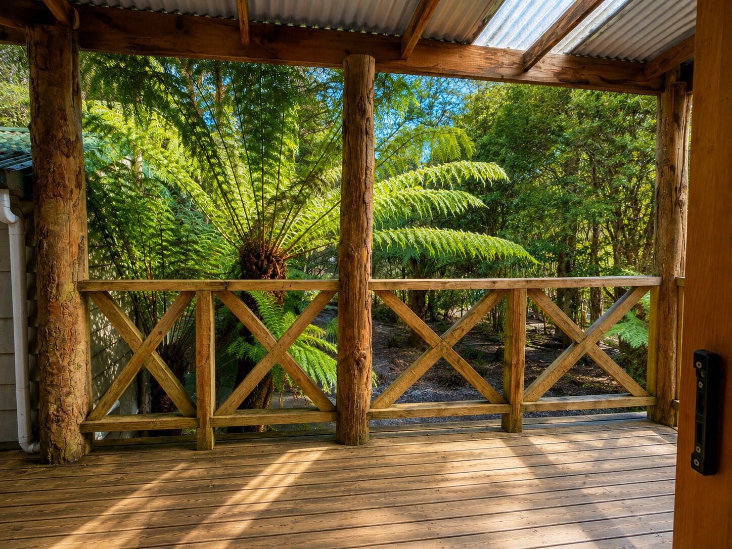 Un terrazza in legno con ringhiera, immersa nel verde e circondata da alberi.