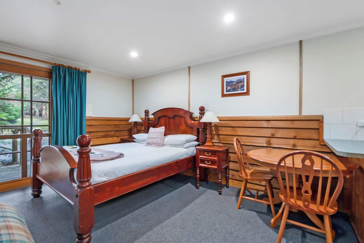 A wooden-framed bed with two bedside tables, a chair, and a small table with a lamp.