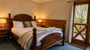 A wooden four-poster bed with a fluffy blanket, a bedside table with a lamp, and a view of trees through a wooden door. - Cradle Forest Inn (Moina)