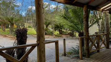 Una terraza de madera con un sendero de grava que lleva a una zona cubierta, rodeada de varios árboles y plantas.