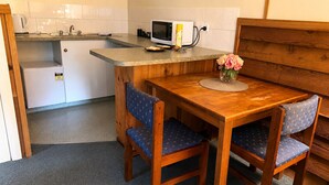 Cocina compacta con microondas, tostadora y lavaplatos. Hay una mesa de madera con sillas y un jarrón con flores.