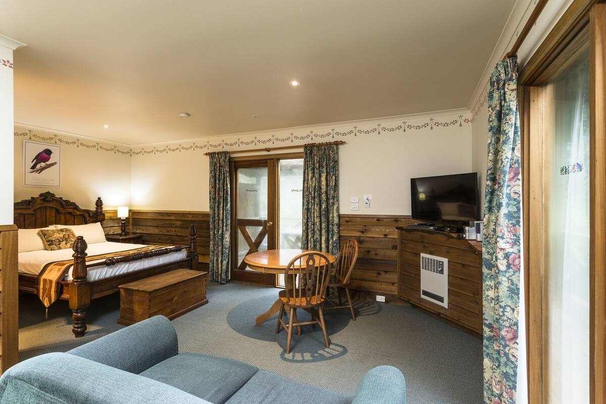 A cozy room with a wooden bed, a sofa, a dining table with chairs, a TV, and a window with curtains.