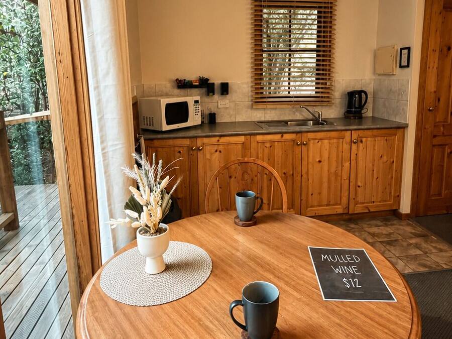 Une table de salle à manger en bois, avec un set de table, deux tasses et un panneau indiquant que du vin chaud est proposé pour 12 dollars.