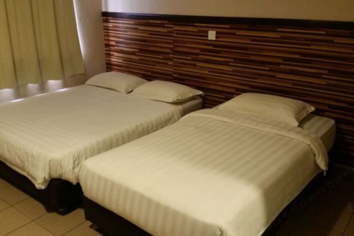 A hotel room with two beds, each with a striped bedspread and pillows. The room has a wooden headboard and a window with curtains.
