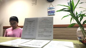 A reception desk with a menu board displaying room rates and a notice about the Tourism Tax Act 2017. - Iskandar Sinsuran Guesthouse (Kota Kinabalu)