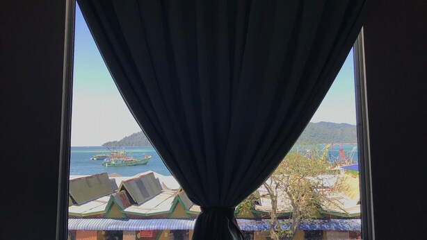 A window with a view of boats and buildings across a body of water. - Iskandar Sinsuran Guesthouse (Kota Kinabalu)
