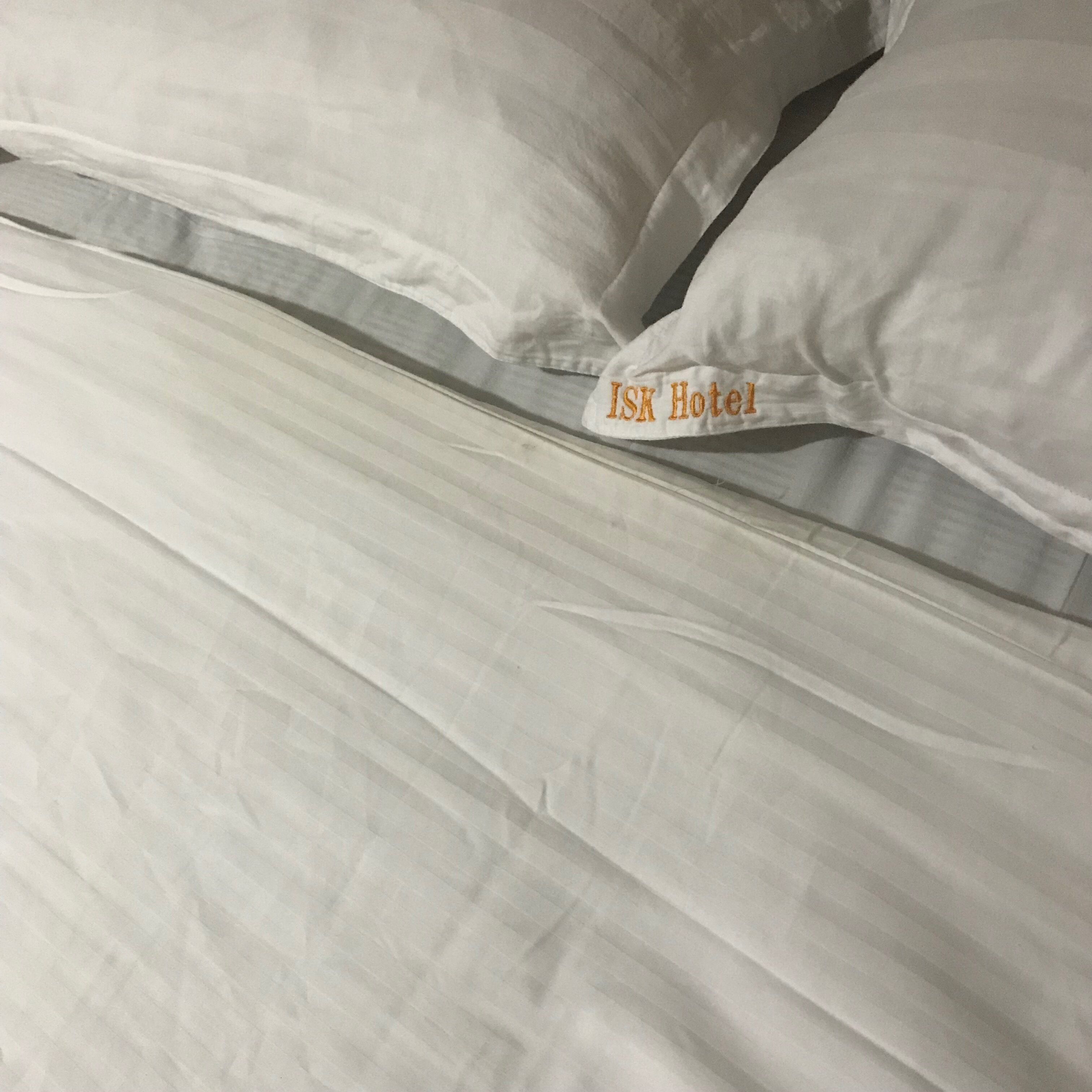 A bed with white bedding and a visible tag reading "ISK Hotel".
