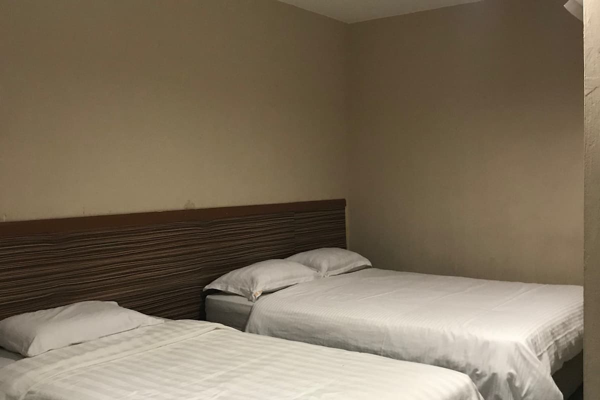 Een hotelkamer met twee eenpersoonsbedden, effen muren en een houten hoofdeinde.