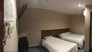 A small hotel room with two single beds, a wooden headboard, a desk with a telephone, and a door. - Iskandar Sinsuran Guesthouse (Kota Kinabalu)