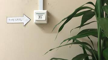 A wall-mounted door exit sign with a keyhole symbol, a directional arrow sign pointing to the right, and a potted plant to the right.