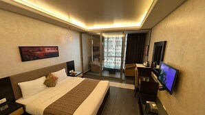 A hotel room with a large bed, a desk with a flat-screen TV, a chair, a sofa, a sliding door to a balcony, and a painting on the wall. - Elite Hotel & Spa (Beirut)