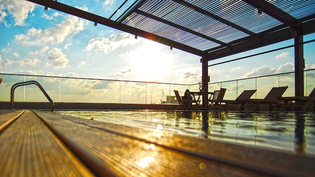 An indoor swimming pool with a view of the sky and clouds, a metal roof, and lounge chairs. - Elite Hotel & Spa (Beirut)