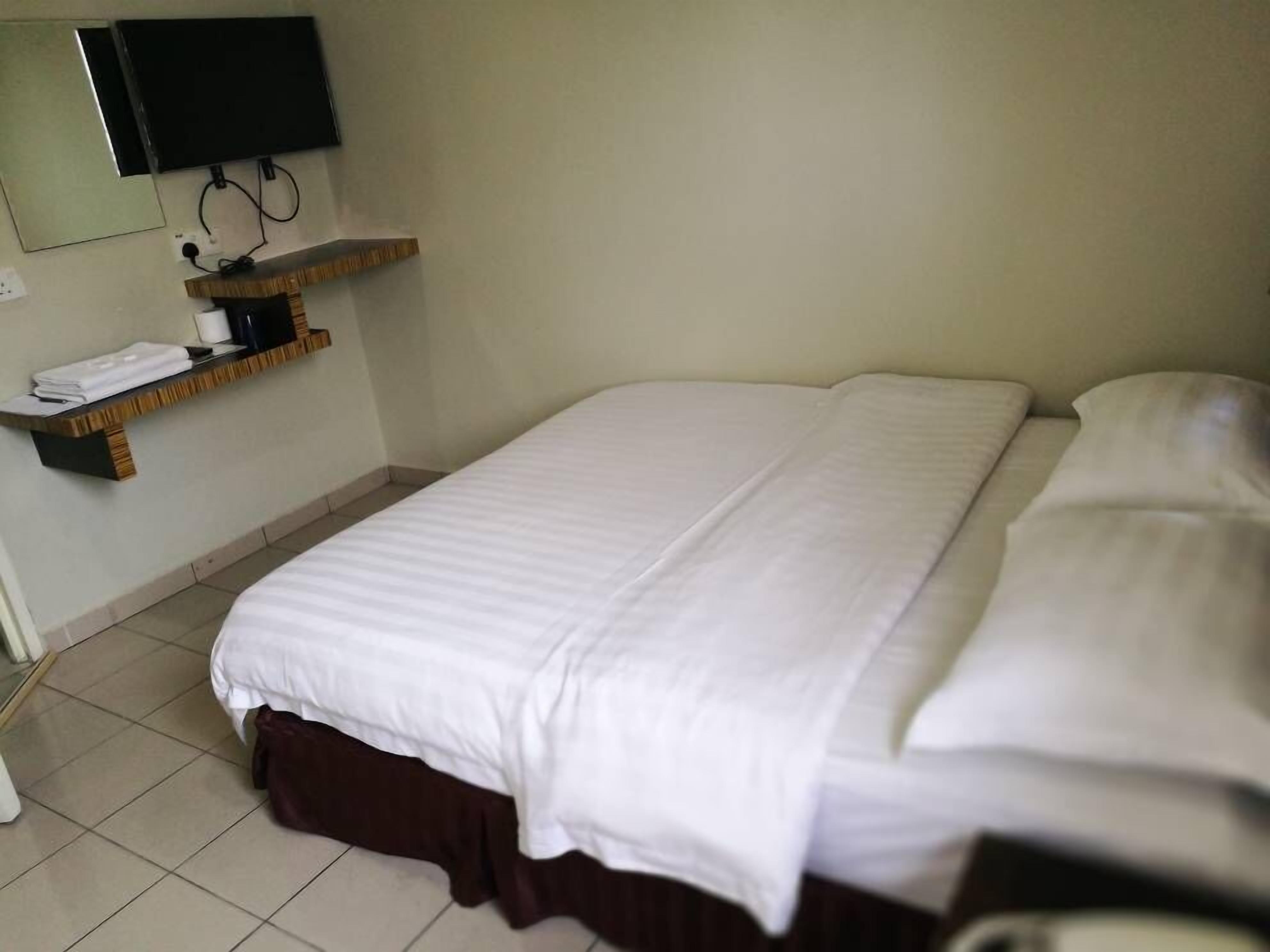 A hotel room with a bed, a TV mounted on the wall, and a shelf with towels.