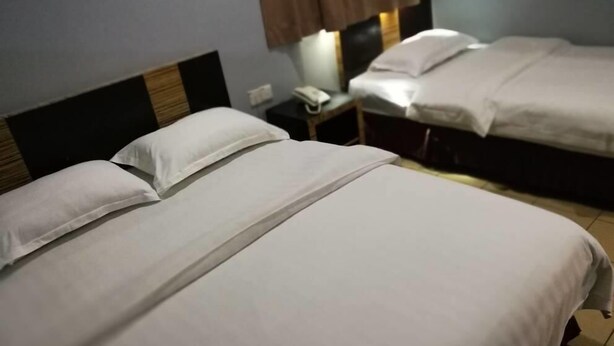 A hotel room with two beds, each with white bedding and a wooden headboard. There is a nightstand with a phone and a lamp. - Hotel Traveller (Kota Kinabalu)
