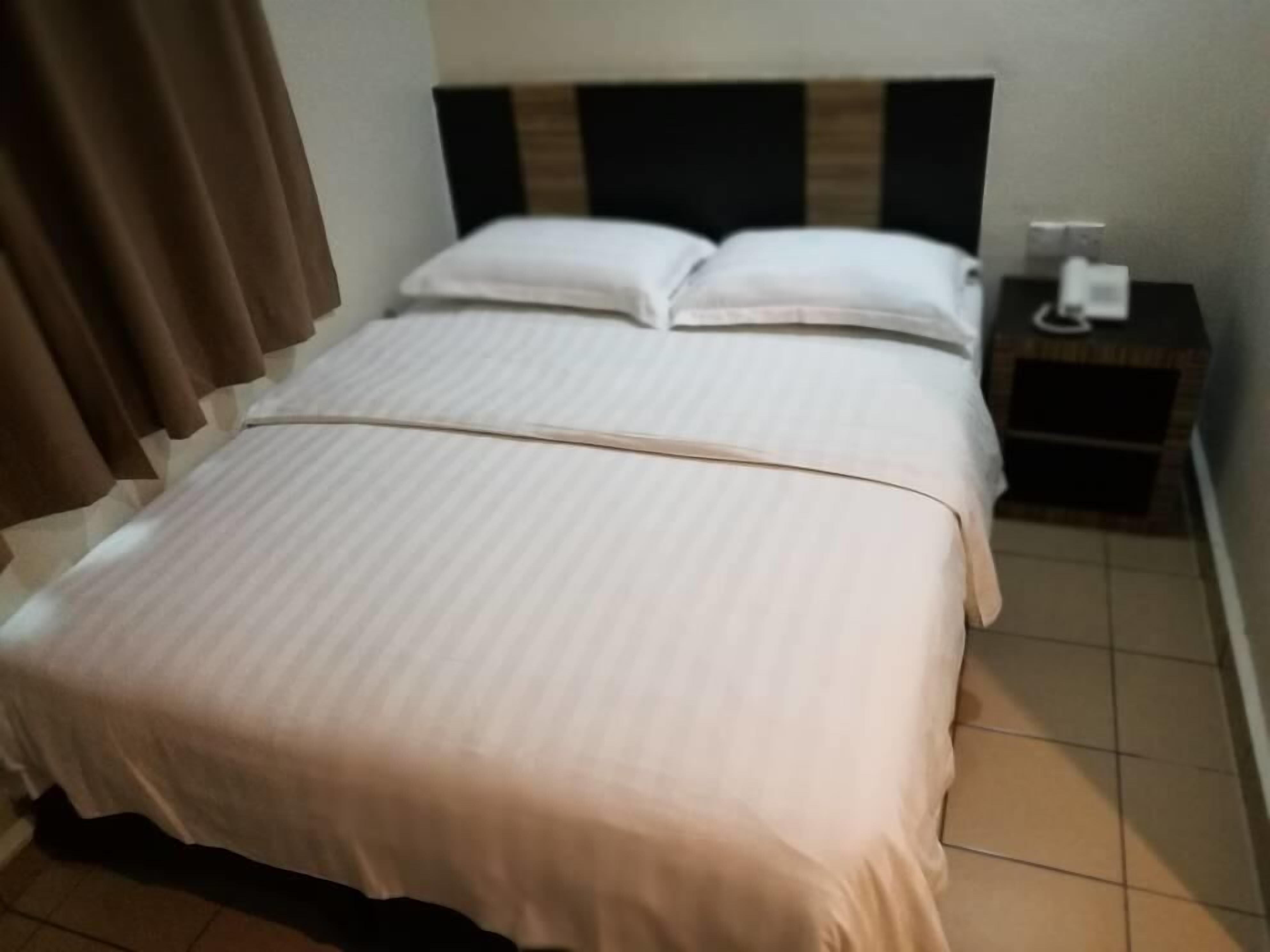 A neatly made bed with a striped bedspread and two pillows, a bedside table with a lamp, and a window with brown curtains.
