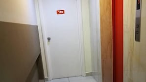 A hallway with a white door marked "110", a red elevator, and a tiled floor. - Hotel Traveller (Kota Kinabalu)