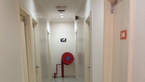 A narrow, well-lit hallway with white walls and doors on either side. A red fire hose reel is mounted on the wall near the center. - Hotel Traveller (Kota Kinabalu)
