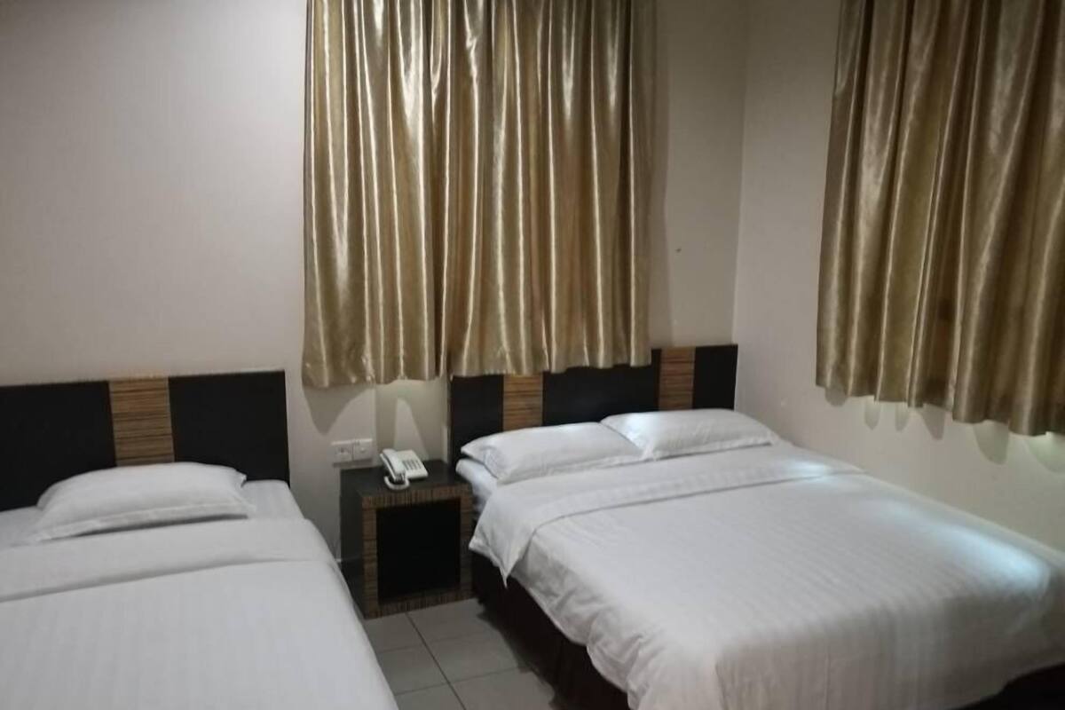 Ein Hotelzimmer mit zwei Einzelbetten, einem Nachttisch mit Telefon und Vorhängen an den Fenstern.