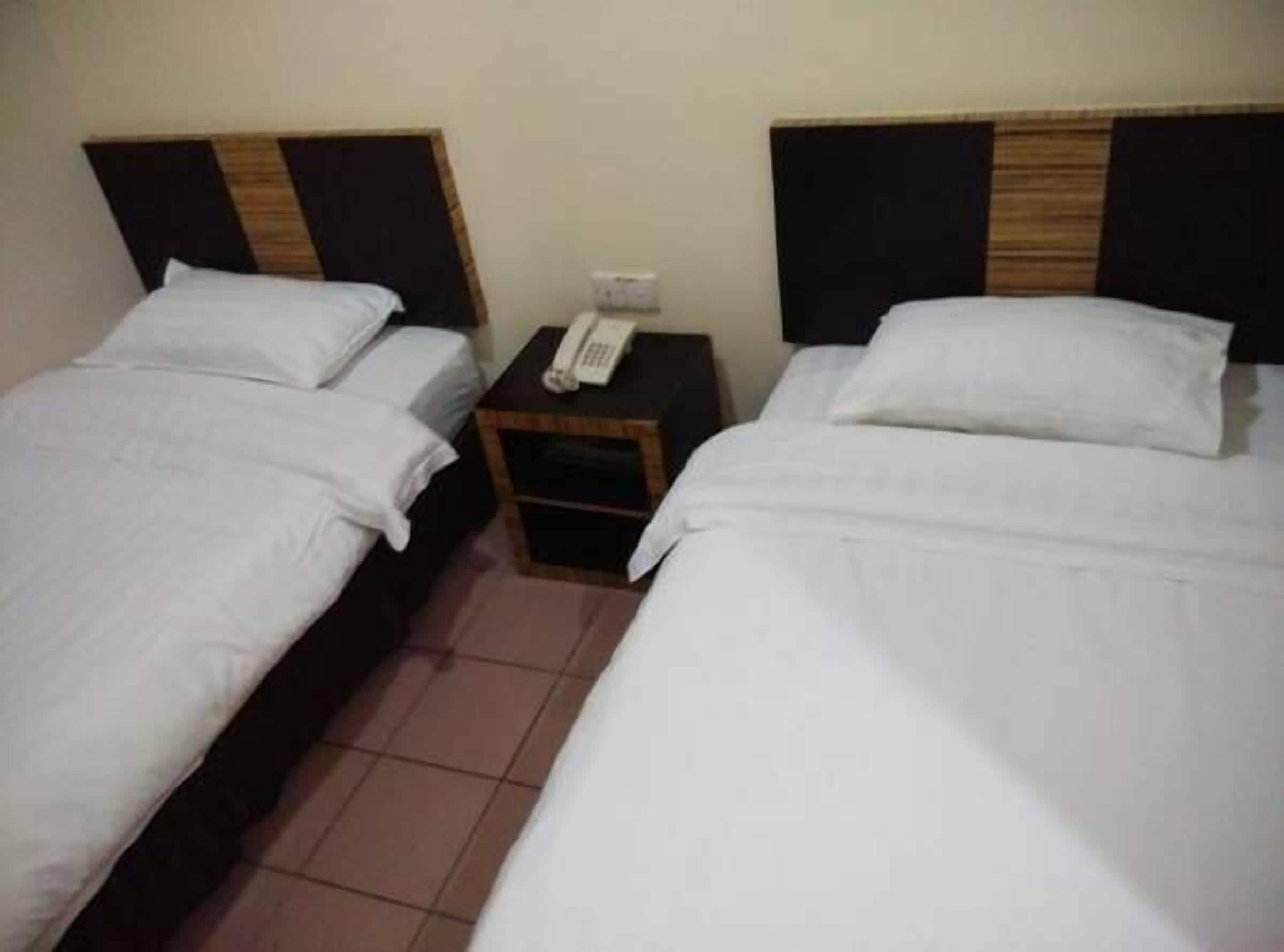 A hotel room with two single beds, a nightstand with a telephone, and a tiled floor.