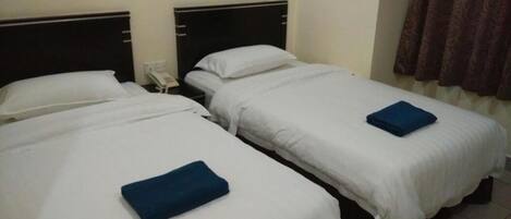 Una habitación de hotel con dos camas individuales, cada una con ropa blanca y una toalla azul. Hay un teléfono en la mesita de noche entre las camas.