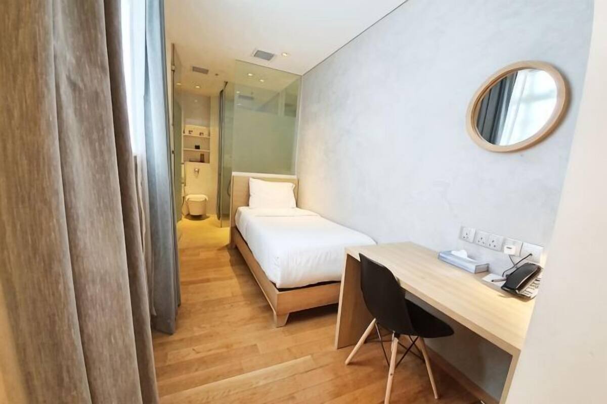 A hotel room with a bed, desk, and chair, a round mirror, and a view of the hallway.