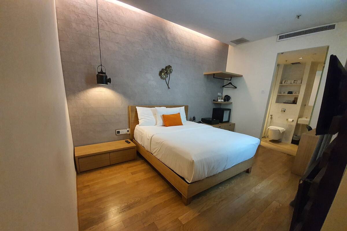 A modern bedroom with a wooden bed, a bedside table, a nightstand, a wall-mounted shelf, and a television.