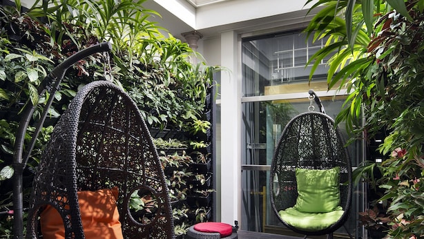 A modern outdoor seating area with wicker chairs and ottomans, surrounded by lush greenery and a glass ceiling. - Hotel Clover 769 North Bridge Road (Singapore)