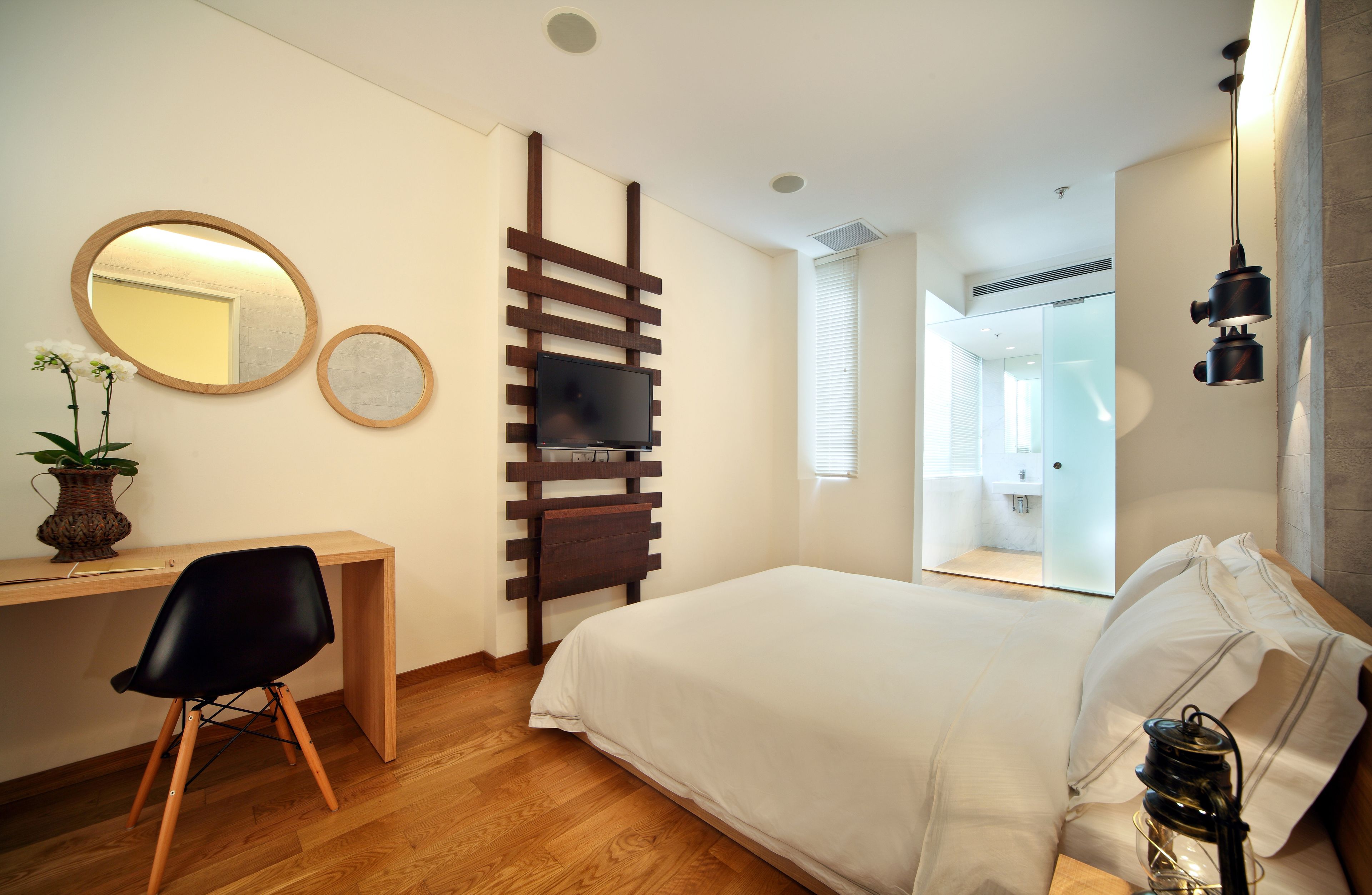 Habitación de hotel moderna con un escritorio de madera, una cama grande, un televisor montado en una pared de listones de madera y una planta en maceta.