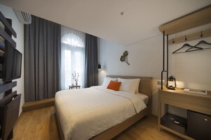 Una habitación de hotel con cama, escritorio con lámpara, televisión y armario.