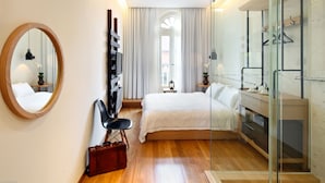 A modern hotel room with a bed, a glass shower enclosure, a wooden floor, a round mirror, and a black chair. - Hotel Clover 769 North Bridge Road (Singapore)