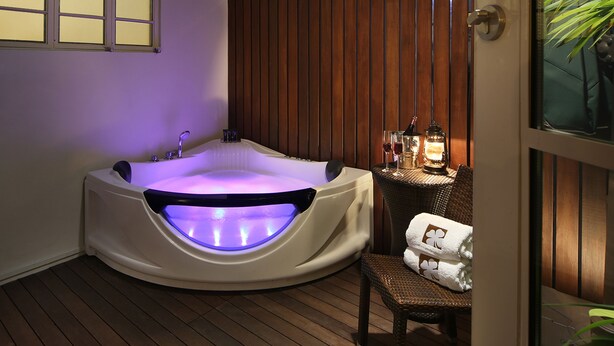 A hot tub with a built-in light, a wooden fence, and a chair with towels. - Hotel Clover 769 North Bridge Road (Singapore)