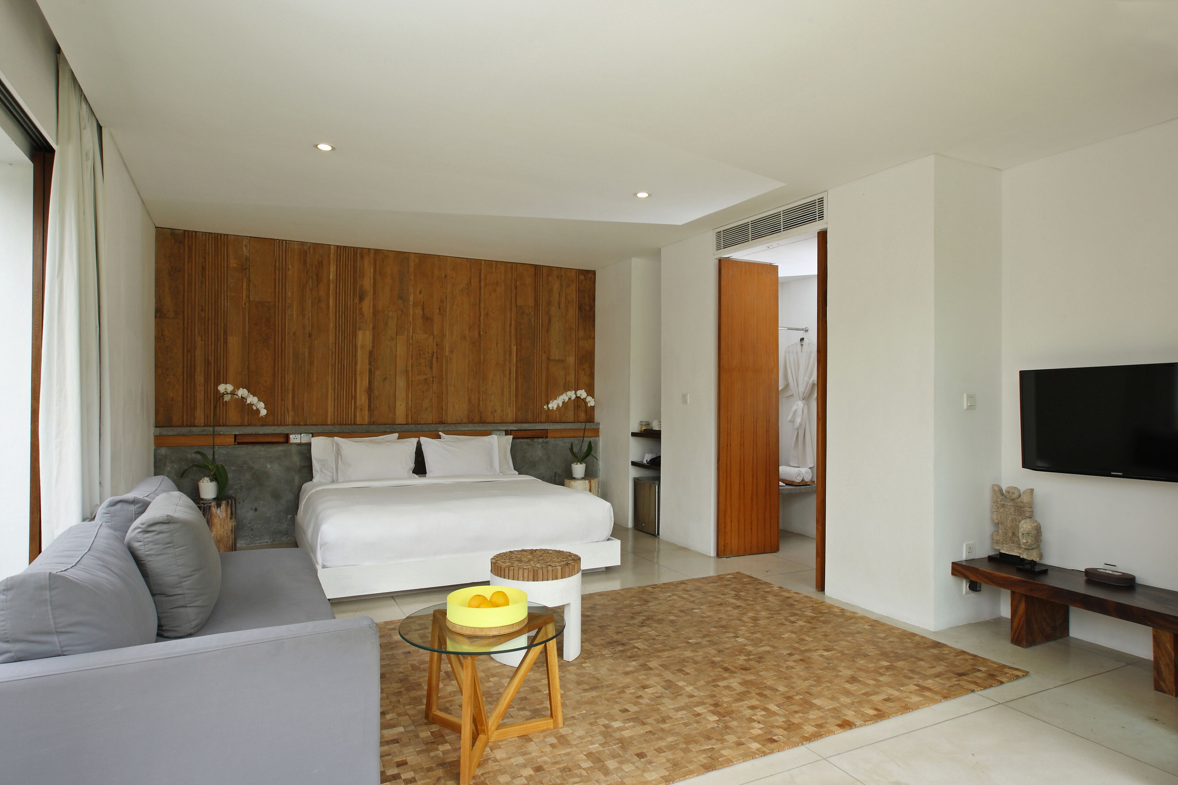 Une chambre moderne avec un grand lit, un canapé, une télévision et une tête de lit en bois.