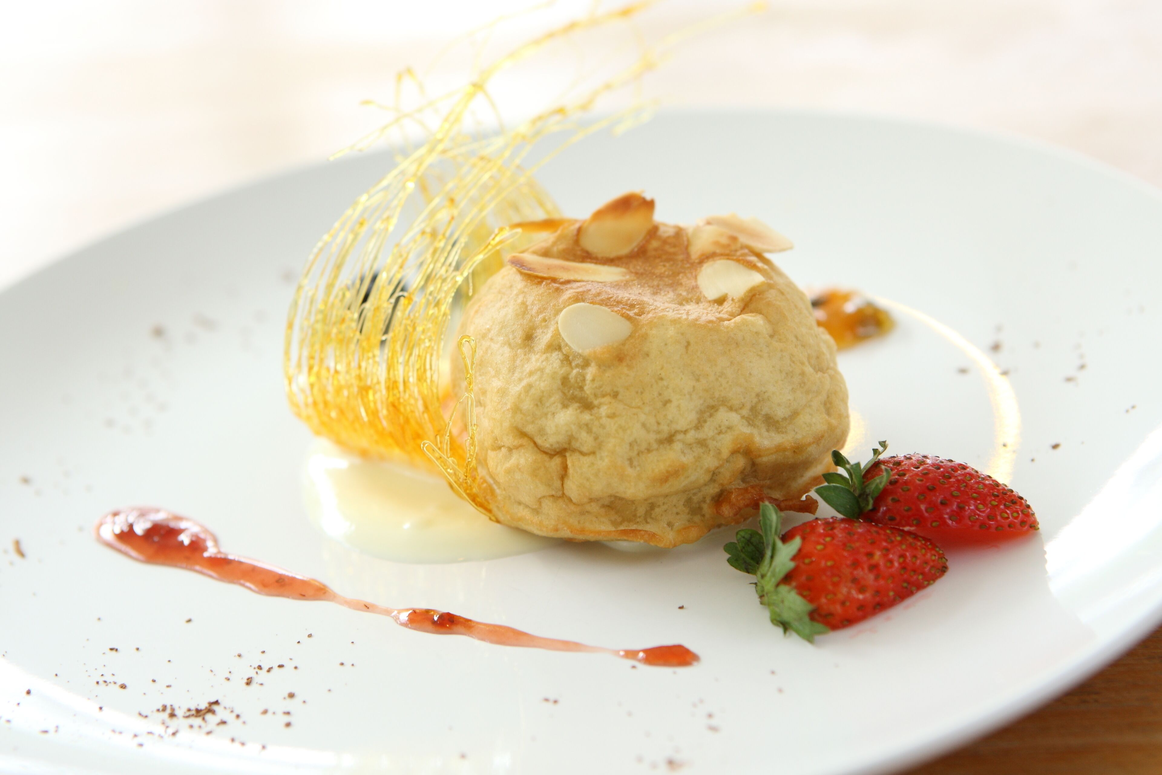 Un postre en un plato con un hojaldre dorado, almendras y fresas.