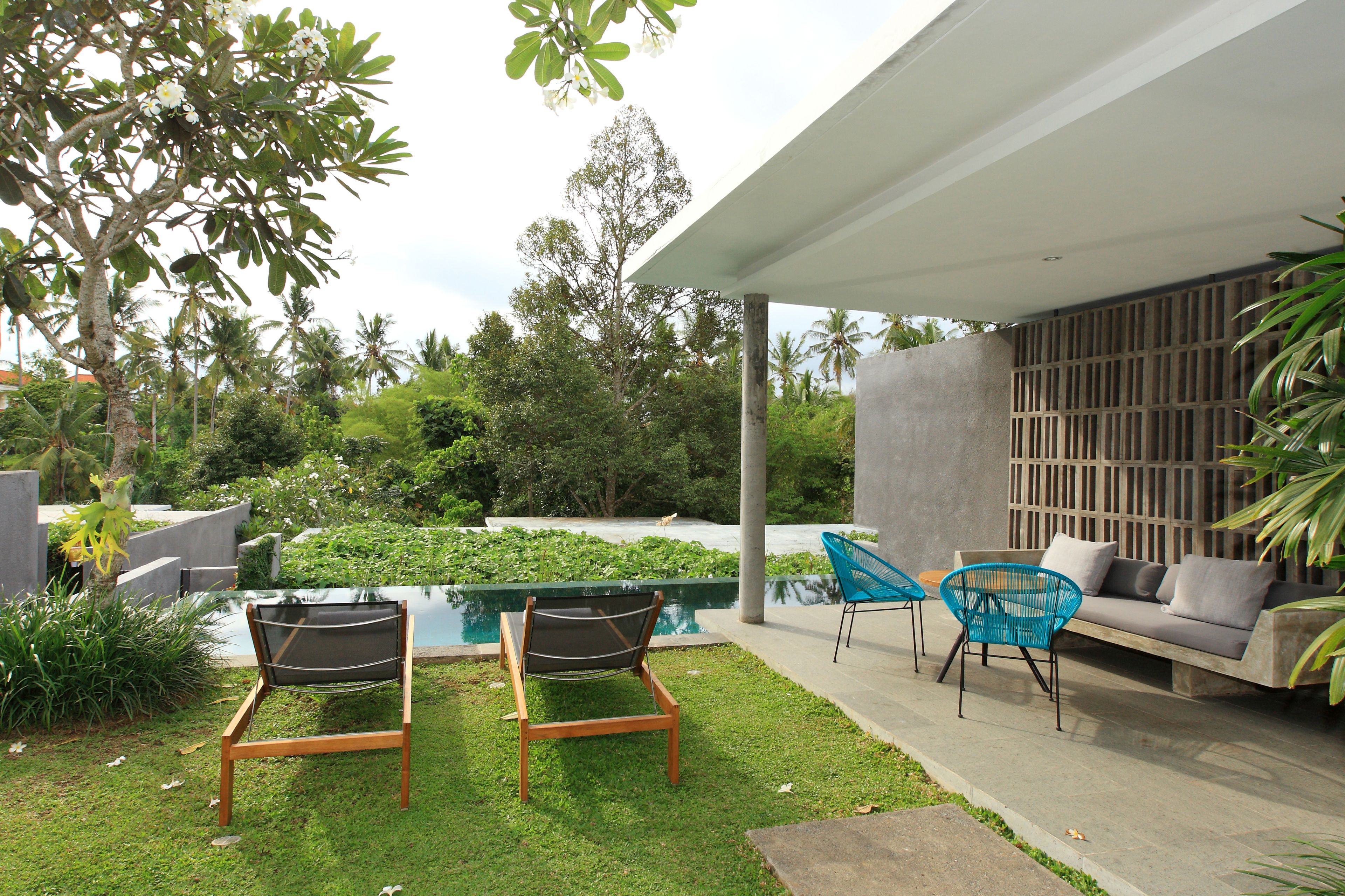 Un patio moderno al aire libre con piscina, dos sillones de descanso, un sofá y una valla de madera.
