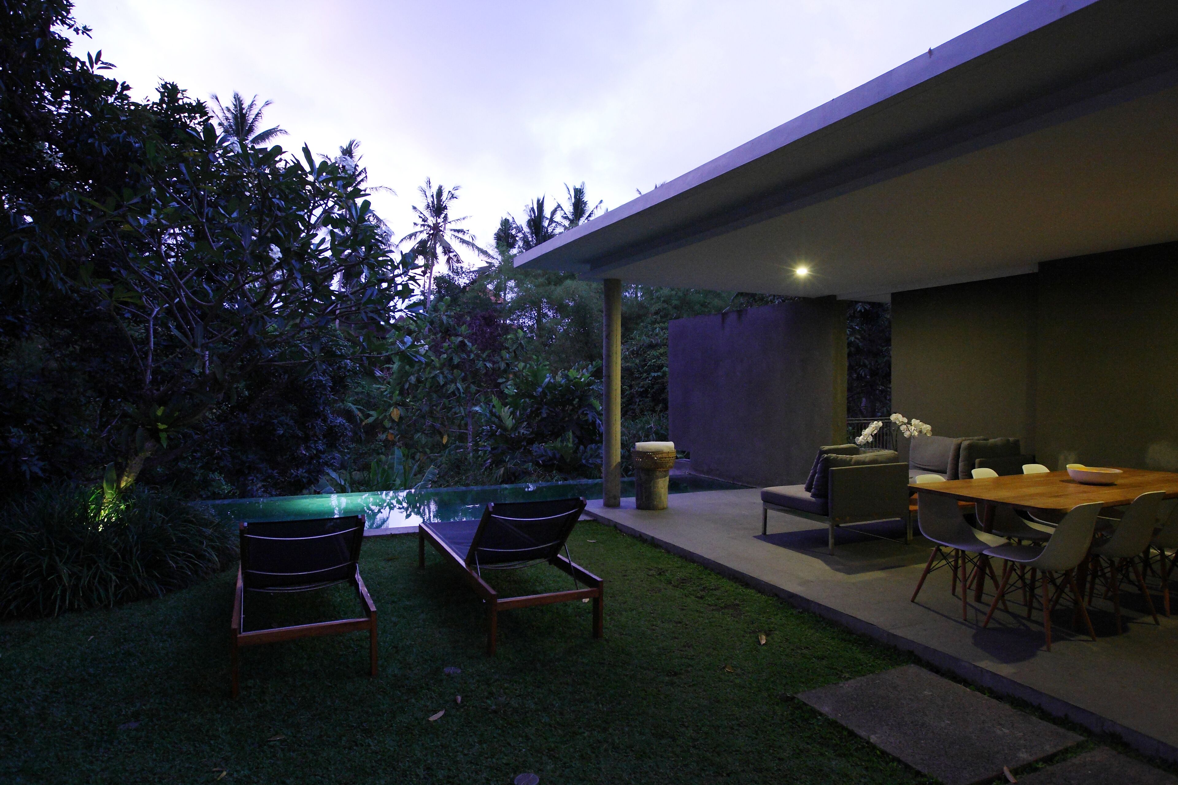 Un patio moderno al aire libre con piscina, sillones de descanso y zona de comedor.
