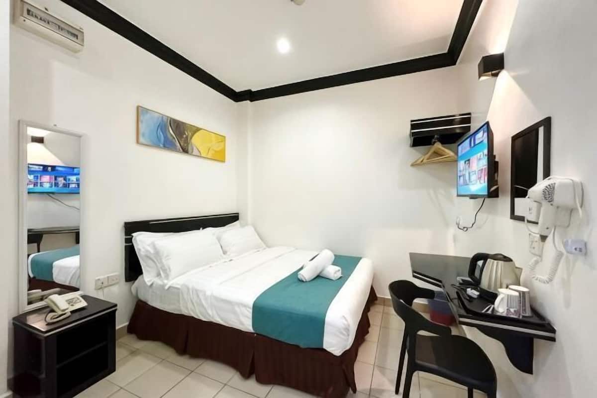 A hotel room with a bed, a desk, a chair, a TV, a mirror, and a telephone.