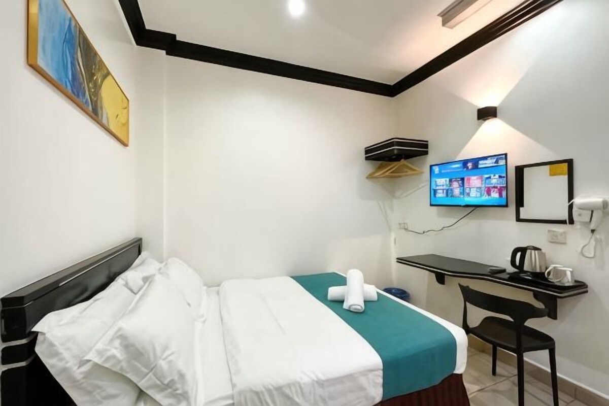 A hotel room with a bed, desk, chair, TV, and a painting on the wall.