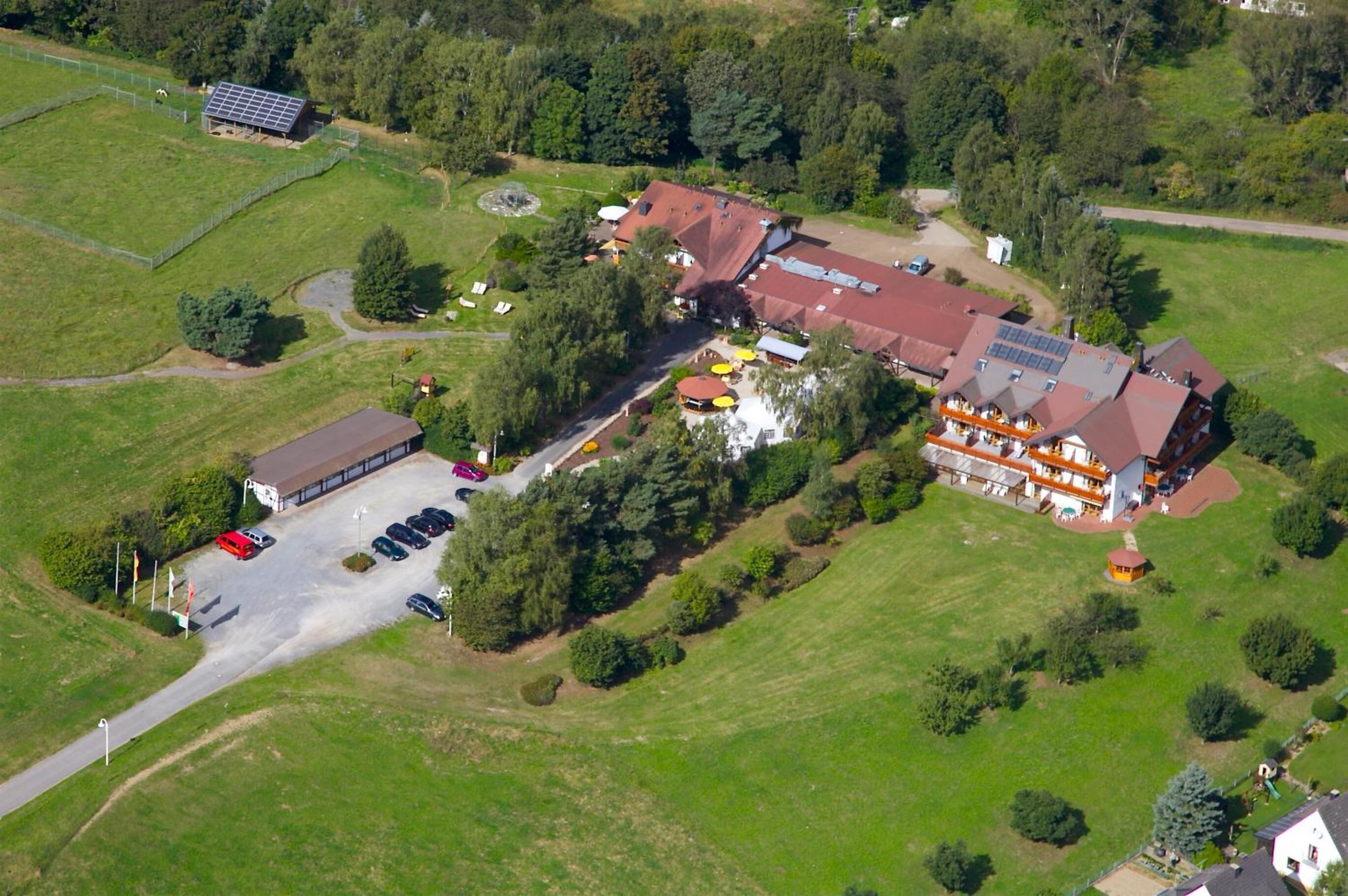 Luchtbeeld van een hotel met meerdere gebouwen, parkeerplaatsen en omliggend groen.