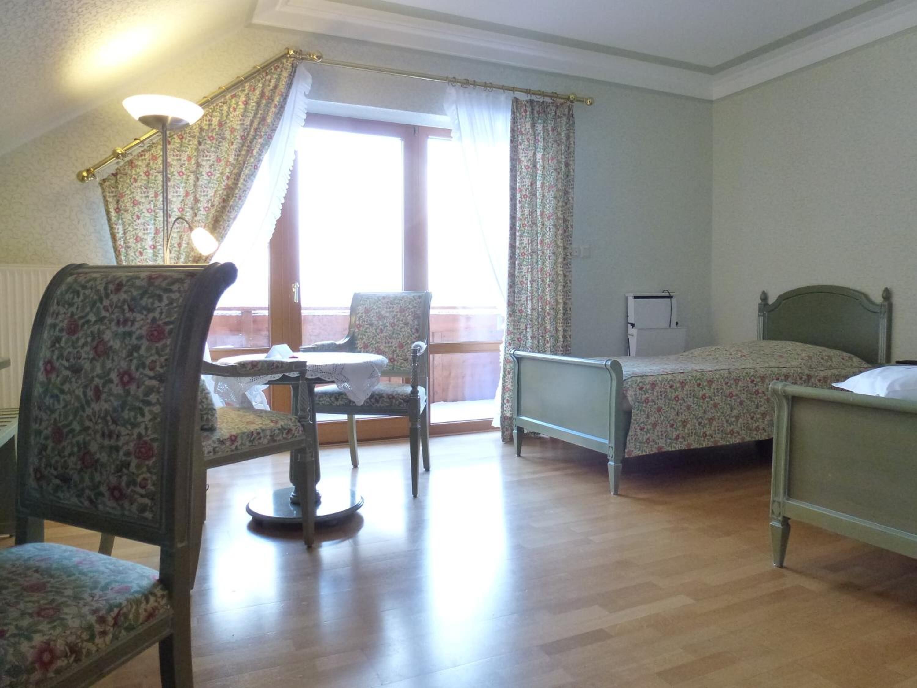 A room with a bed, a chair, a table, and a window with curtains.