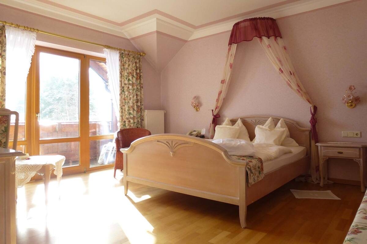A bedroom with a bed, a chair, a nightstand, and a window with curtains.