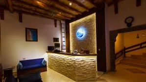 A reception area with a stone wall, a blue sofa, a wooden reception desk, and a clock on the wall. - Zinbad Hotel (Kas)