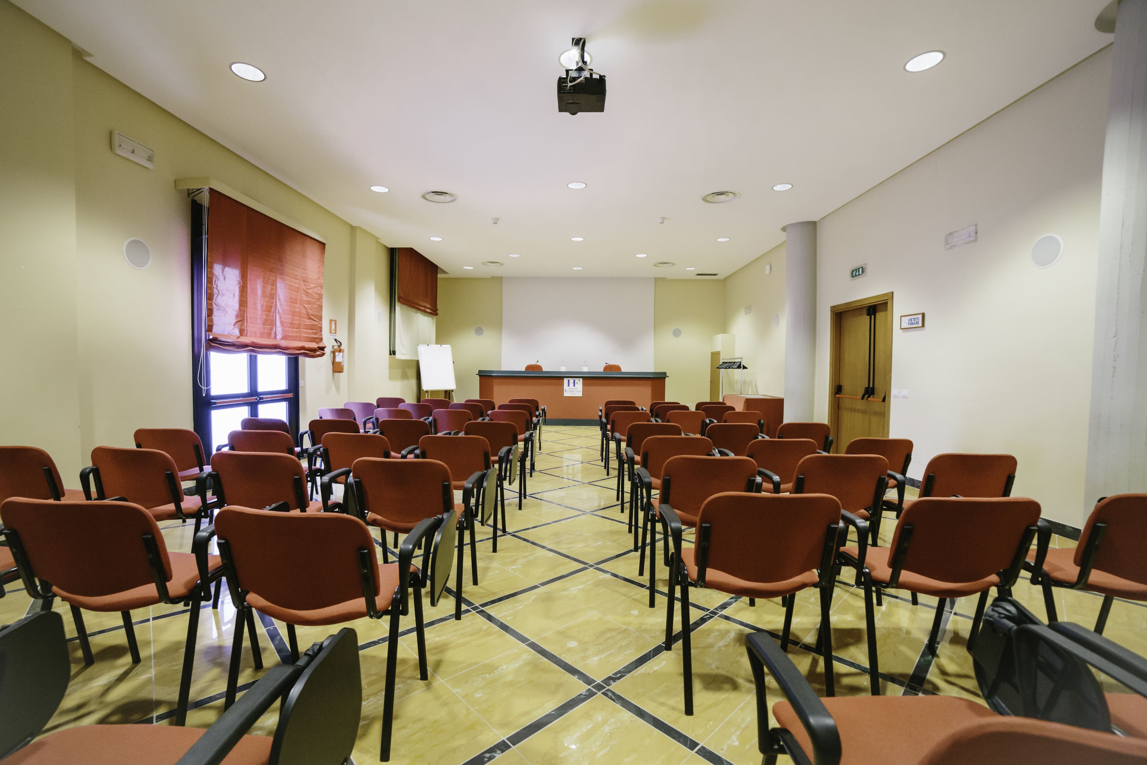 Un salón de conferencias con filas de sillas, un atril y un proyector en el techo.