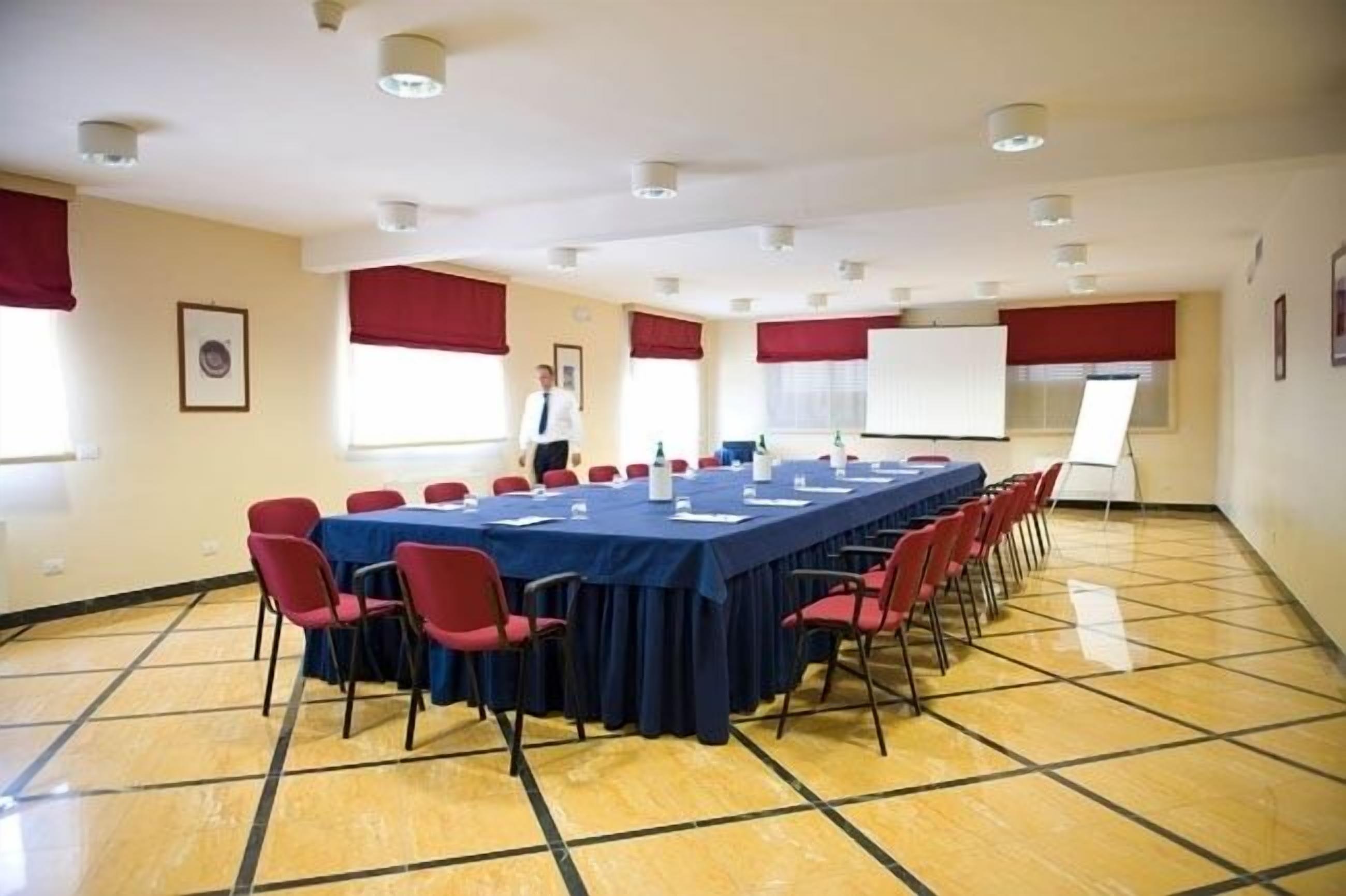 Un salón de conferencias con una larga mesa, sillas rojas y una pizarra.