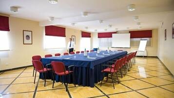 Una sala conferenze con un lungo tavolo, sedie rosse e una lavagna.