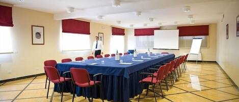 Un salón de conferencias con una larga mesa, sillas rojas y una pizarra.