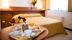 A hotel room with a neatly made breakfast tray on a wooden table, a bed with a yellow bedspread, and a vase with flowers on the nightstand. - Hotel Federiciano (Valenzano)